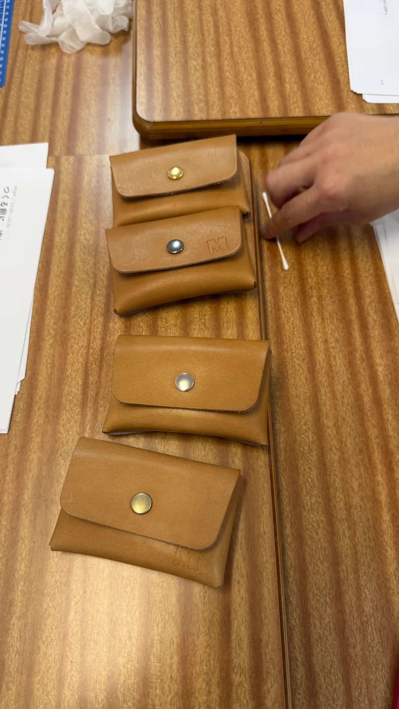 ワークショップで参加者が制作した革のカードケースを、木の机に置いた様子